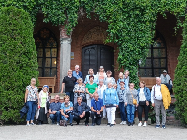 grupa kobiet i mężczyzn pod budynkiem który opleciony jest zielonym bluszczem.