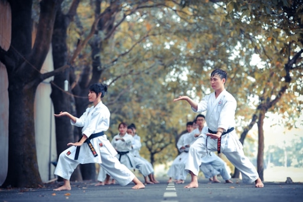 kobiety i mężczyźni stoją w dwóch rzędach. Z przodu po lewej kobieta, po prawej mężczyzna. stoją w jednej z pozycji karate.